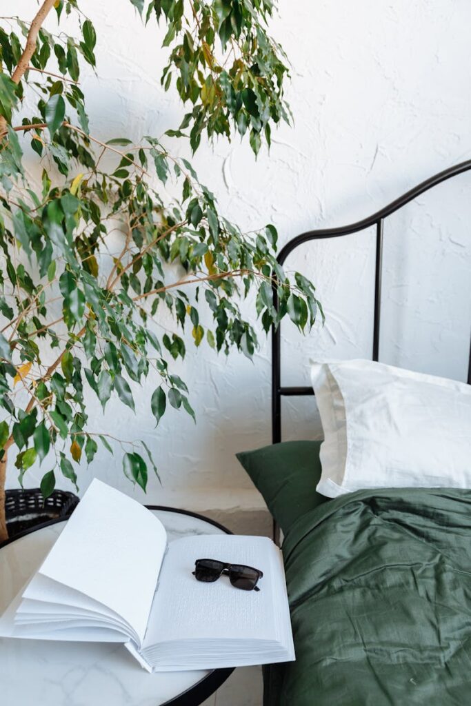 Tranquil bedroom scene with open book and sunglasses on a table near a cozy bed.